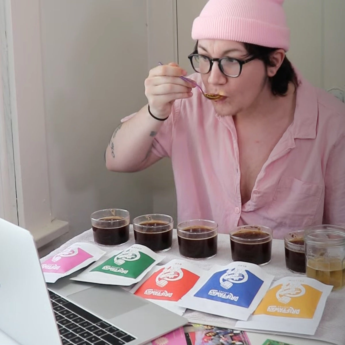 Person in a pink shirt and hat sitting at a table with coffee cups and colorful cards.