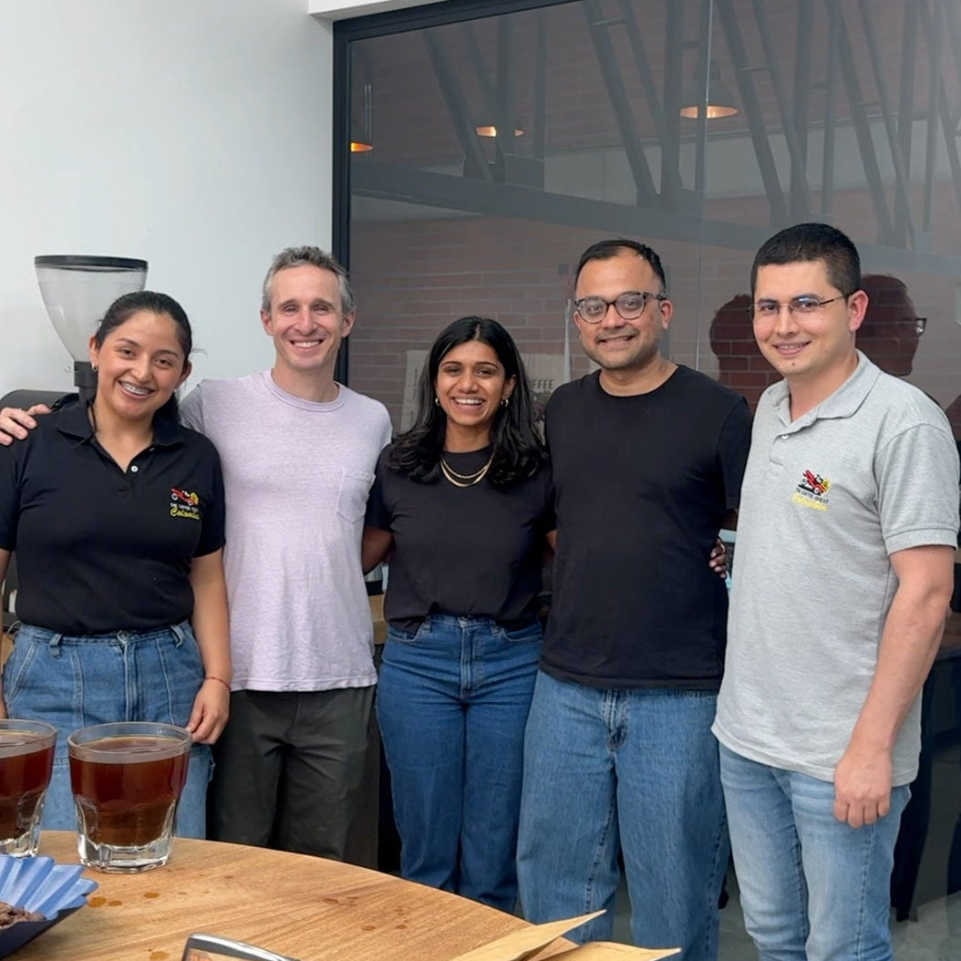 Five people posing together in a modern office setting with a wooden table and drinks.